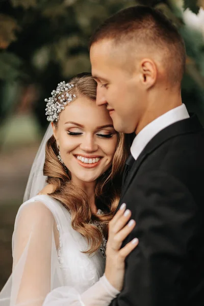 couple in love in the autumn park. Blonde bride in a wedding dress with sleeves. The groom is in a classic black suit, white shirt and tie. Rear view