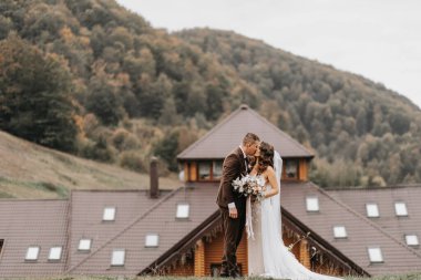 Gelin ve damat, dağların arka planında ve bir restoranda öpüşürler. Dağlarda düğün gezisi