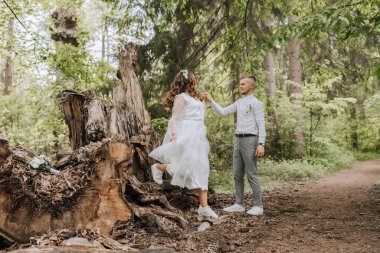 Ormanda düğün yürüyüşü. Damat gelinin elini tutar ve büyük bir ağaç kütüğünün üzerinde dururlar. Dikey fotoğraf