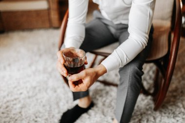 Bir otel odasında genç bir işadamı sandalyeye oturur ve viskisini bardaktan içer. Harika dairelerde dinlenin. Otelde damadın sabahı. Erkek elleri yakın.