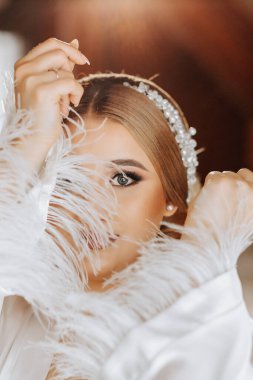 Güzel bir gelinin portresi bir otelde, geniş kollu, zarif beyaz bir bornozla. Düğün hazırlıkları..