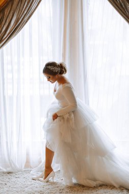 Beyaz gelinlik içinde güzel bir gelinin portresi ve otel odasında uzun bir tren. Gelin ayakkabılarını giyer