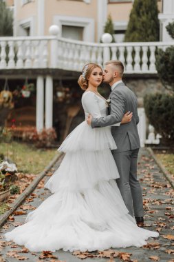 Gelin ve damadın güzel mimarisi ve beyaz parmaklıkları olan bir parkta yürüyüşü. Uzun trenli gelin.