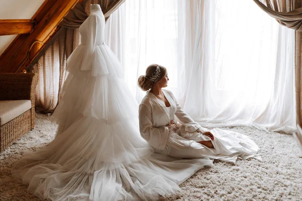portrait of a beautiful bride in a hotel near a wedding dress. Preparation for the wedding ceremony. Horizontal photo.