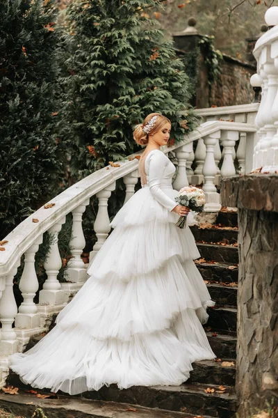 Portrait of a bride in a wedding dress with a train on elegant steps. Full length photo. Wedding in a top location