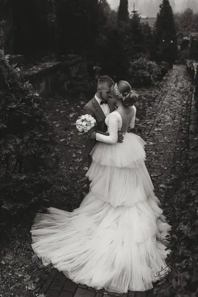 Full-length portrait of the bride and groom in the garden near tall trees. Wedding walk in the garden. black and white photo