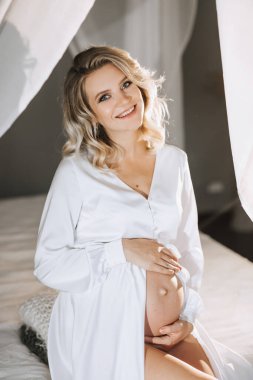 Beyaz bornozlu, beyaz bir trenle peçeli güzel hamile bir kadının stüdyo portresi.