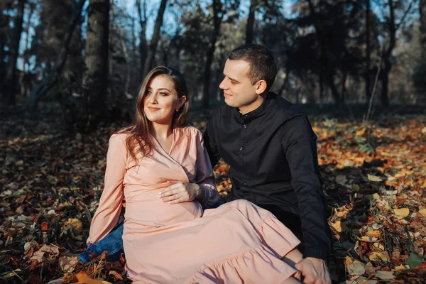 一个男人在秋天的森林里躺在一片黄色的叶子上 用手摸着他怀孕的妻子的肚子 丈夫在怀孕期间的支助 — 图库照片