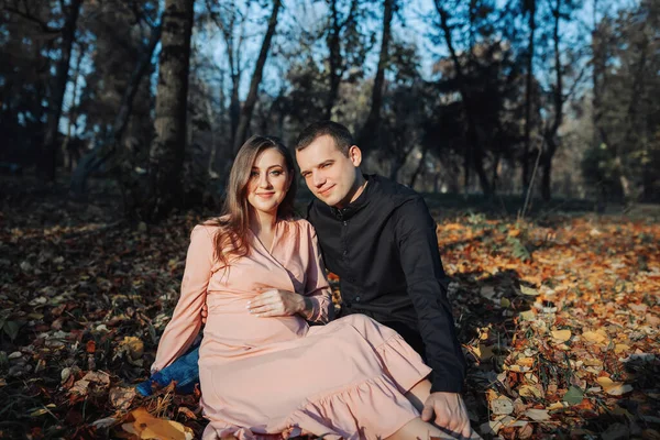 一个男人在秋天的森林里躺在一片黄色的叶子上 用手摸着他怀孕的妻子的肚子 丈夫在怀孕期间的支助 — 图库照片