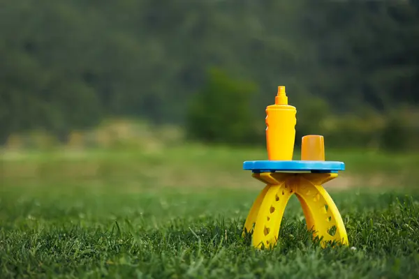 绿山背景上的防晒霜 儿童座椅上有防晒霜和绿色草坪的橙色塑料瓶 — 图库照片