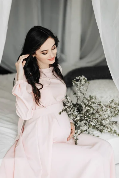 Piękna Kobieta Ciąży Długimi Ciemnymi Włosami Różowej Sukience Siedzi Łóżku — Zdjęcie stockowe