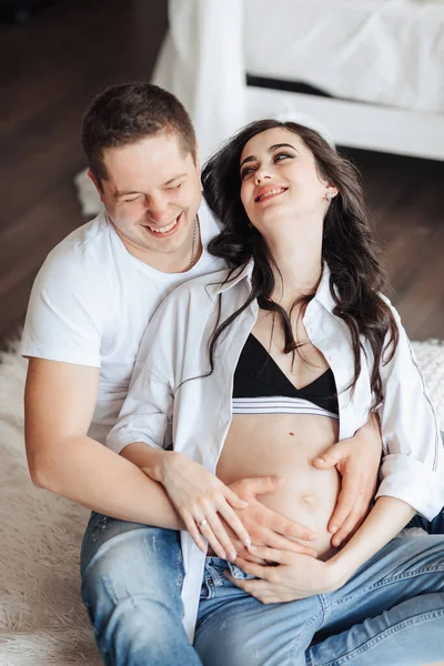 ジーンズの現代美しい妊婦と自宅で夫とシャツを着て 抱きしめ 抱きしめ キスをしました そして待機の概念 妊娠中の女性の美しさ — ストック写真