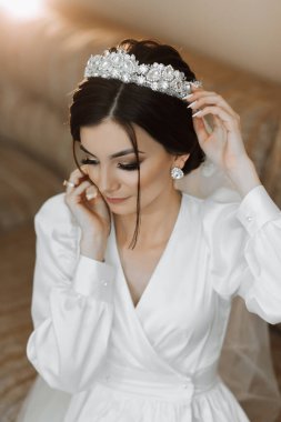 Kafasında taç olan bornozlu güzel bir kızın portresi. Moda, cazibe, kavramlar. Gelinin sabahı, bornozlu gelin kanepede oturuyor..