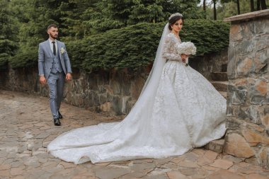 Gelinin elinde uzun bir tren ve bir buket ortanca çiçekli güzel beyaz elbisesi vardı. Arkasında klasik takım elbiseli bir damat var.