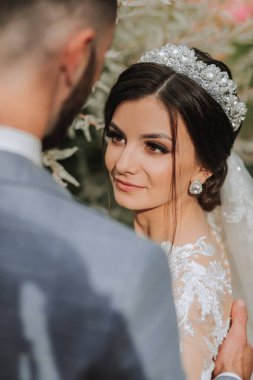 Gelinin kolları ve kafasında bir taç ve ellerinde bir buket ortanca ile güzel beyaz bir elbisesi vardı.