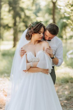 Modaya uygun bir damat ve beyaz elbiseli hoş bir gelin. Taze çiçeklerden yapılmış bir taç takıyorlar. Parkta, bahçede, ormanda gülüyorlar. Düğün fotoğrafı, gülümseyen yeni evlilerin portresi..