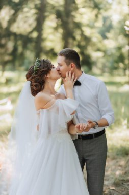 Modaya uygun bir damat ve beyaz elbiseli hoş bir gelin. Taze çiçeklerden yapılmış bir taç takıyorlar. Parkta, bahçede, ormanda gülüyorlar. Düğün fotoğrafı, gülümseyen yeni evlilerin portresi..