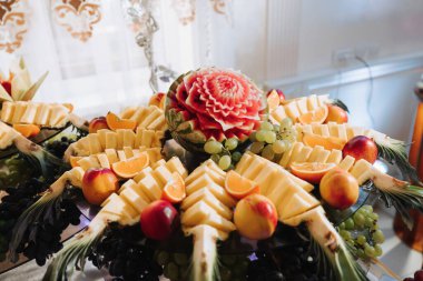 Çeşitli meyve süslemeleri olan bir masa. Karpuz oyma, ananas dilimleri, üzümler, portakal