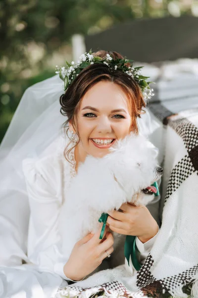 彼女のプードル犬と庭にポーズする彼女の頭の上の新鮮な花のティアラと白いドレスの若いエレガントな花嫁 — ストック写真