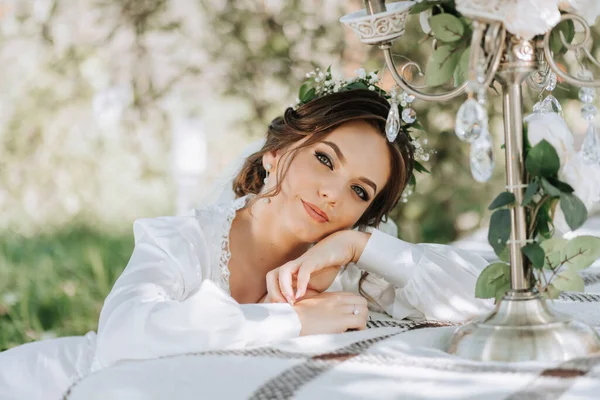 Portrait of the bride in the garden. The beautiful bride is wearing a white dress and a tiara of fresh flowers on her head