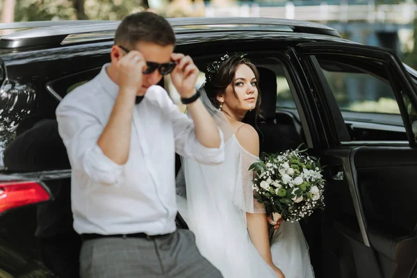 結婚式の肖像画 白いシャツと弓のネクタイと黒い車の近くの花束が付いているブルネットの花嫁のスタイリッシュな花の写真 — ストック写真