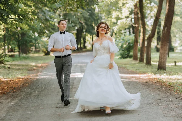 結婚式のカップル 幸せな花嫁とグロムは 結婚式の場所に公園で走っています ウェディングコンセプト — ストック写真