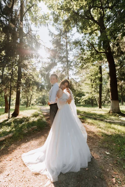 时尚的新郎和可爱的新娘 身穿白衣 头戴鲜花 在公园 森林里嬉笑 婚纱照 新婚夫妇面带微笑的肖像 — 图库照片