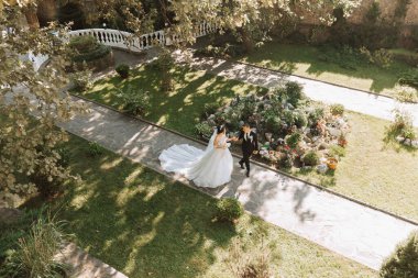 Genç ve güzel bir çift el ele tutuşup bahçede yürüyor, yukarıdan çekilmiş bir fotoğraf.