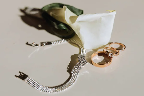 a boutonniere of calla flowers, a gold wedding ring on the table, a silver bracelet