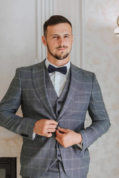 A stylish groom with a beard is preparing for the wedding ceremony. Groom\'s morning. A businessman fastens his jacket. The groom is getting ready in the morning before the wedding ceremony