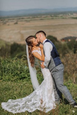 Gelin ve damat, yaz dağlarının arka planında sarılıp öpüşürler. Dağlarda kırsal evlilik kavramı, mutlu bohem yeni evliler..