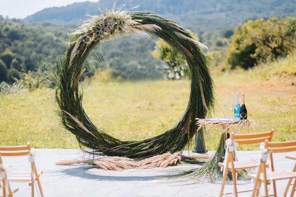The wedding arch in the park is made of dry reeds on the background of the forest in blurred focus. Away wedding ceremony. Decorated chairs for the ceremony