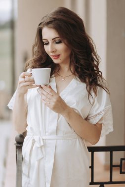 Sabahleyin bornozlu genç bir kadının otel balkonunda durup bir fincan kahveyle manzaranın keyfini çıkarması, olumlu, iyimser, yeni güneşli bir gün.