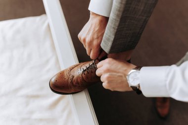 Erkekler için moda. Kahverengi deri ayakkabılarının bağcıklarını bağlayan bir adamın yakın çekimi. Bir işadamı toplantı için hazırlanıyor.