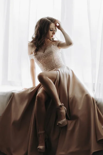 행복한 아름다운 소녀는 창턱에 우아하게 있습니다 호화스러운 베이지색 드레스에 흐르는 — 스톡 사진