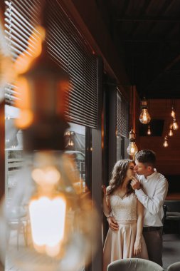 Gülen Avrupalı bir çiftin yan görünüm portresi. Bir kafede eski lambalarla eğleniyor.