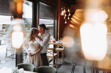 Gülen Avrupalı bir çiftin yan görünüm portresi. Bir kafede eski lambalarla eğleniyor.