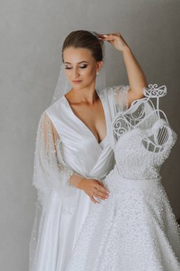 Sabahlık giymiş güzel bir kızın portresi. Moda, cazibe, kavramlar. Gelinin sabahı, bornozlu gelin gelinliğiyle bir mankenin yanında duruyor.