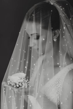 Gelinin elinde çigila ve orkide çiçeklerinden yapılmış damadı için lüks bir buket. Güzel eller ve manikür. Gelin peçenin altında. Siyah beyaz fotoğraf
