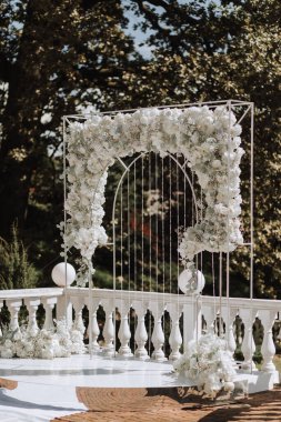Avrupa tarzında modern bir tören. Ormanın arka planında güller olan düğün kemeri. Taze çiçeklerden, çiçeklerden ve kristallerden yapılmış mücevherler. Ön görünüm.