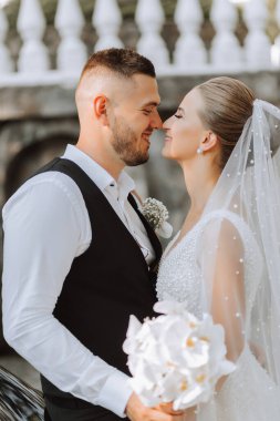 Gelin ve damat güzel bir bahçede ayakta ve kucaklaşıyorlar. Gün batımının geniş açılı fotoğrafı.