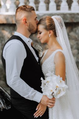 Gelin ve damat güzel bir bahçede ayakta ve kucaklaşıyorlar. Gün batımının geniş açılı fotoğrafı.