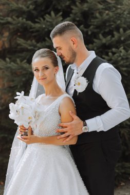 Gelin ve damat güzel bir bahçede ayakta ve kucaklaşıyorlar. Gün batımının geniş açılı fotoğrafı.