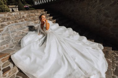 Taştan basamaklarda uzanan, omuzları açık gelinlik içinde genç ve güzel bir gelin. Sert güneş ışığı altında moda çekimi. Fotoğraf yukarıdan çekildi.