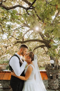 Gelin ve damat güzel bir bahçede ayakta ve kucaklaşıyorlar. Gün batımının geniş açılı fotoğrafı.
