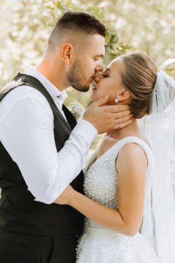 Gelin ve damat güzel bir bahçede ayakta ve kucaklaşıyorlar. Gün batımının geniş açılı fotoğrafı.