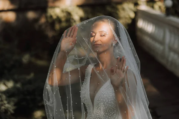 Wedding portrait of the bride. Beautiful blonde bride in a white dress under a long veil in the forest.