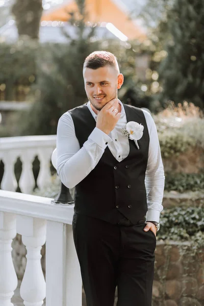 candid portrait of young stylish groom in classic black suit with waistcoat, white shirt