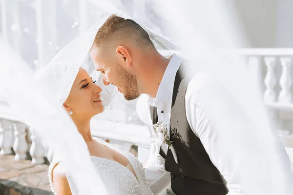 A stylish couple of European newlyweds. Smiling bride in a white dress. The groom, dressed in a classic black suit, white shirt, under a veil. Wedding in nature