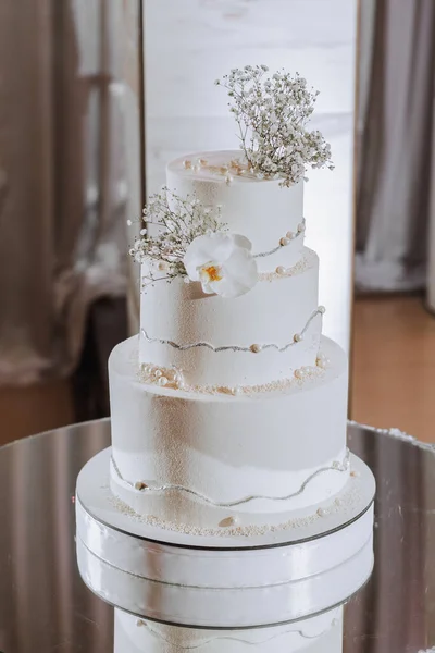 在婚宴大厅的镜面上装饰着兰花和吉普赛花的三层白色结婚蛋糕 — 图库照片
